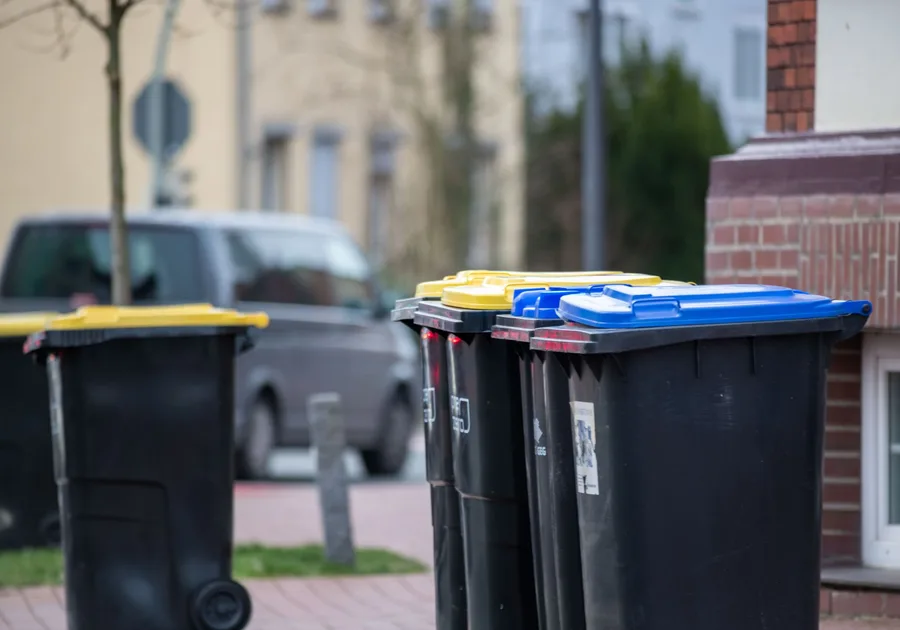 Reihe schwarzer Mülltonnen mit gelben und blauen Deckeln vor einem Wohnhaus