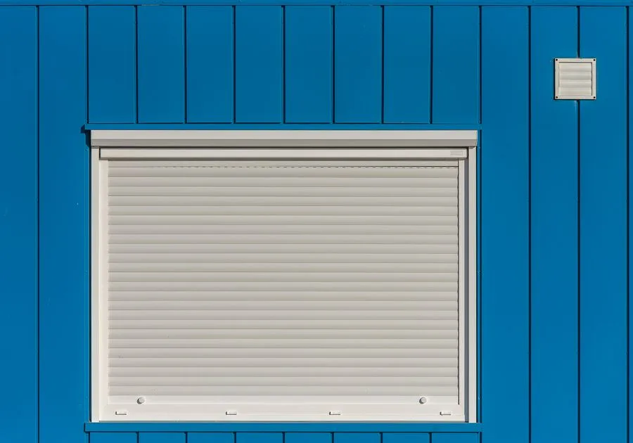 Geschlossener weißer Rollladen an einer blauen Hauswand