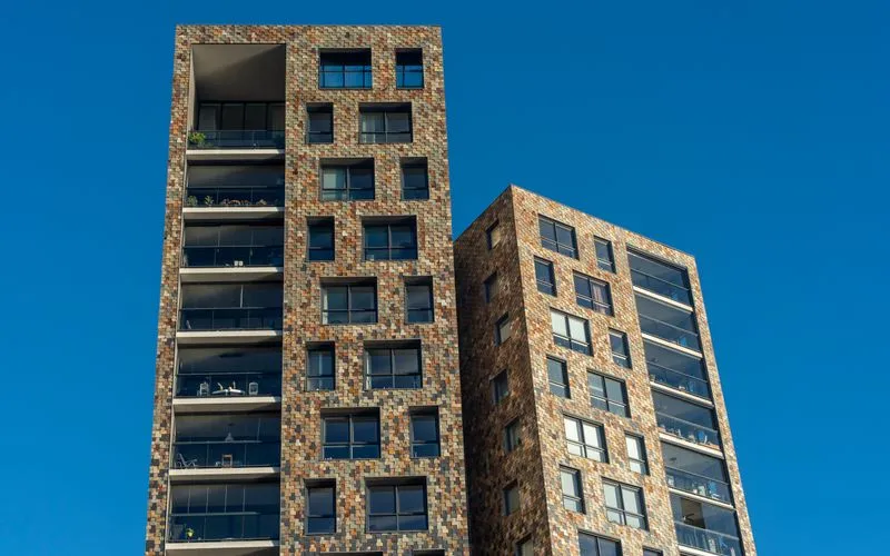 Zwei moderne Wohngebäude mit Backsteinfassade vor blauem Himmel