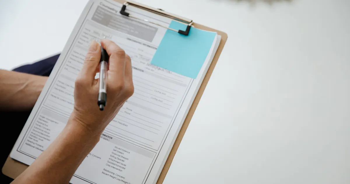 Hand hält einen Stift über ein Klemmbrett mit einer handschriftlichen Checkliste