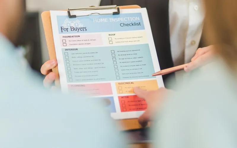 Hände halten eine Checkliste zur Objektkontrolle auf einem Klemmbrett
