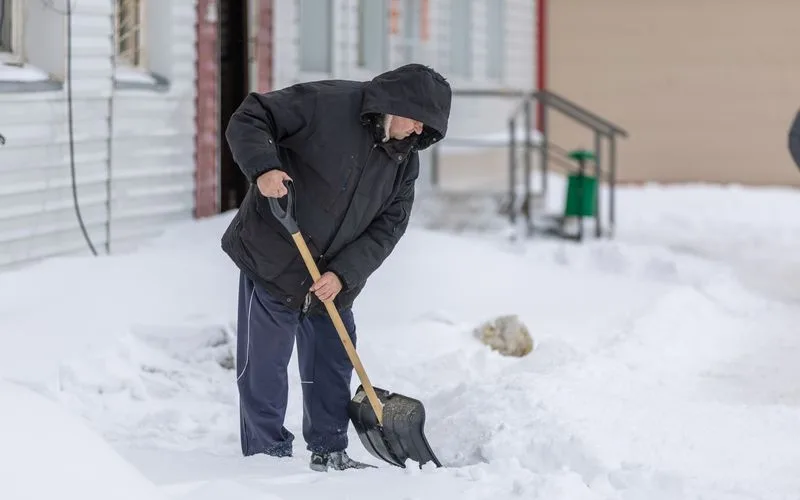 Mann schippt bei winterlichen Temperaturen Schnee mit einer Schaufel