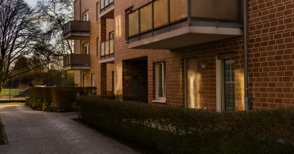 Moderne Mehrfamilienhaus-Fassade mit Balkonen und geschnittener Hecke im Abendlicht
