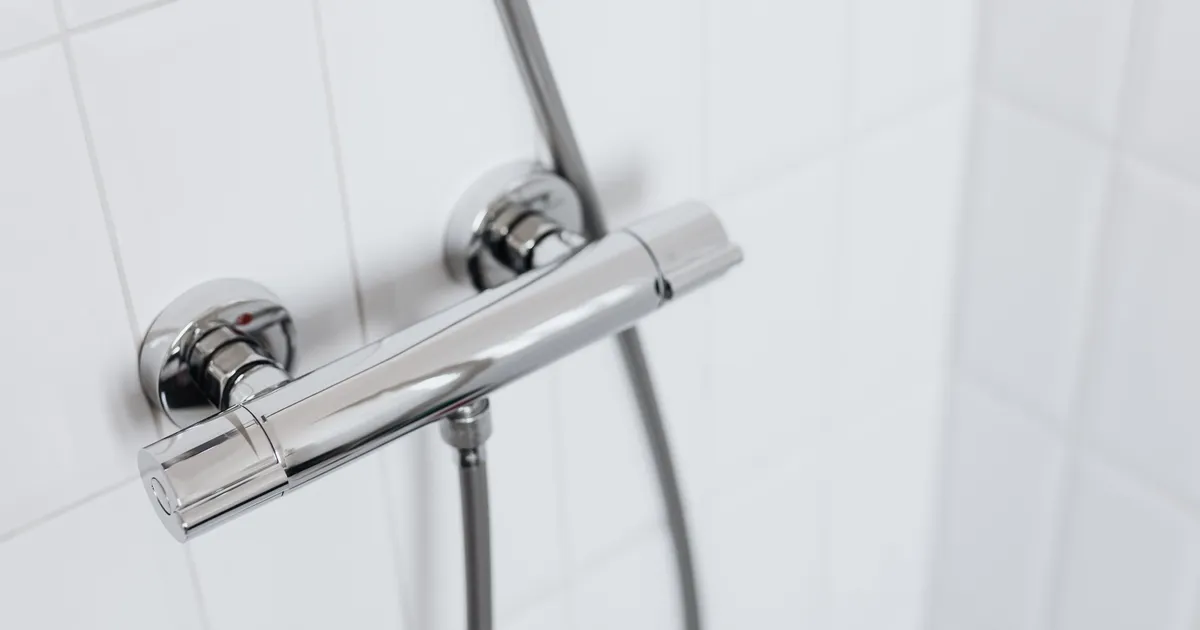 Moderne Chrom-Duscharmatur mit Handbrause an einer weiß gefliesten Wand