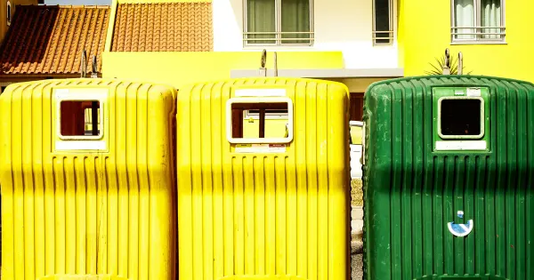 Bunte Recycling- und Mülltonnen vor der sonnigen Fassade eines modernen Wohnhauses
