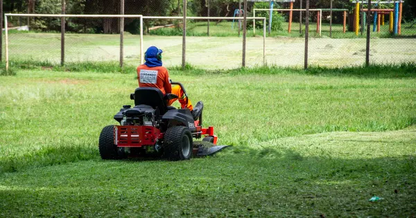 Person fährt mit einem Aufsitzmäher über eine große Rasenfläche