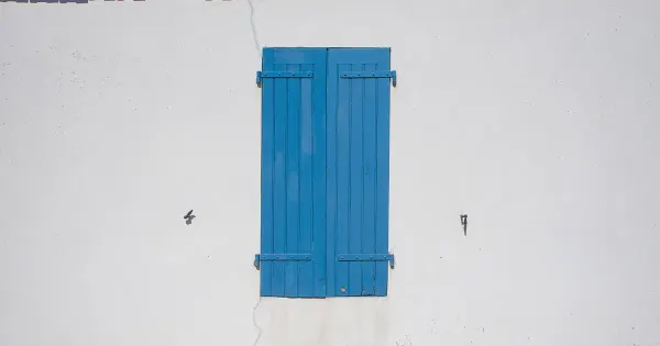 Geschlossener blauer Fensterladen an einer weißen Hauswand mit rotem Ziegeldach