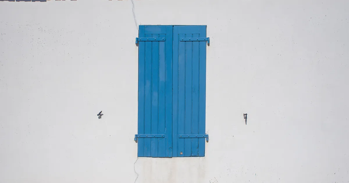 Geschlossener blauer Fensterladen an einer weißen Hauswand mit rotem Ziegeldach